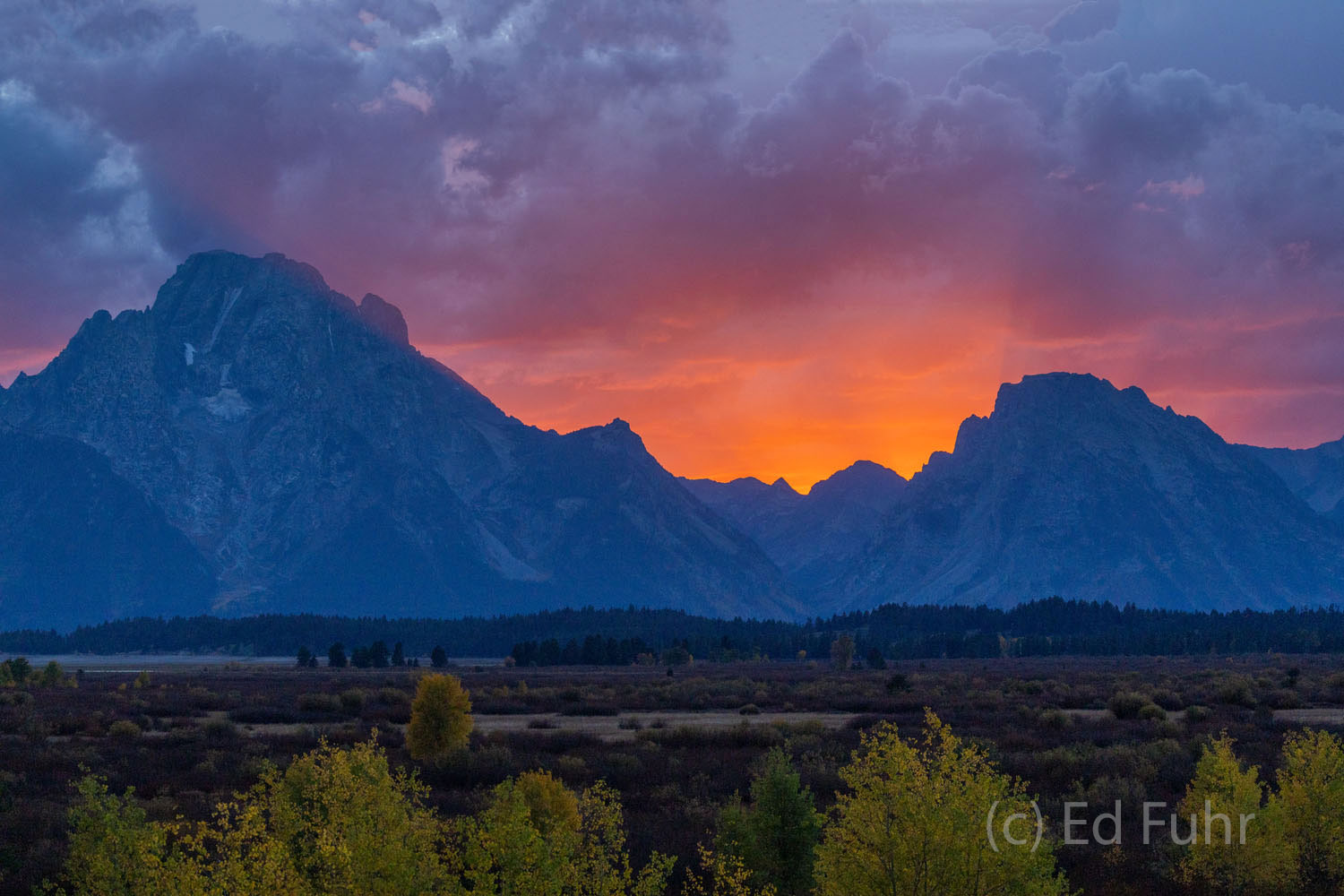 A powerful afternoon thunderstorm has hovered over the Tetons' highest peaks.  As the sun approaches the horizon an orange glow...