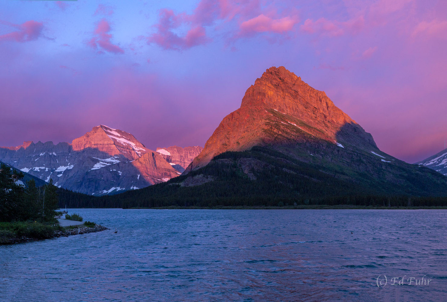 A beautiful pink sky and golden lights paints Mt. Grinnell and mt. Gould above Swiftcurrent Lake.