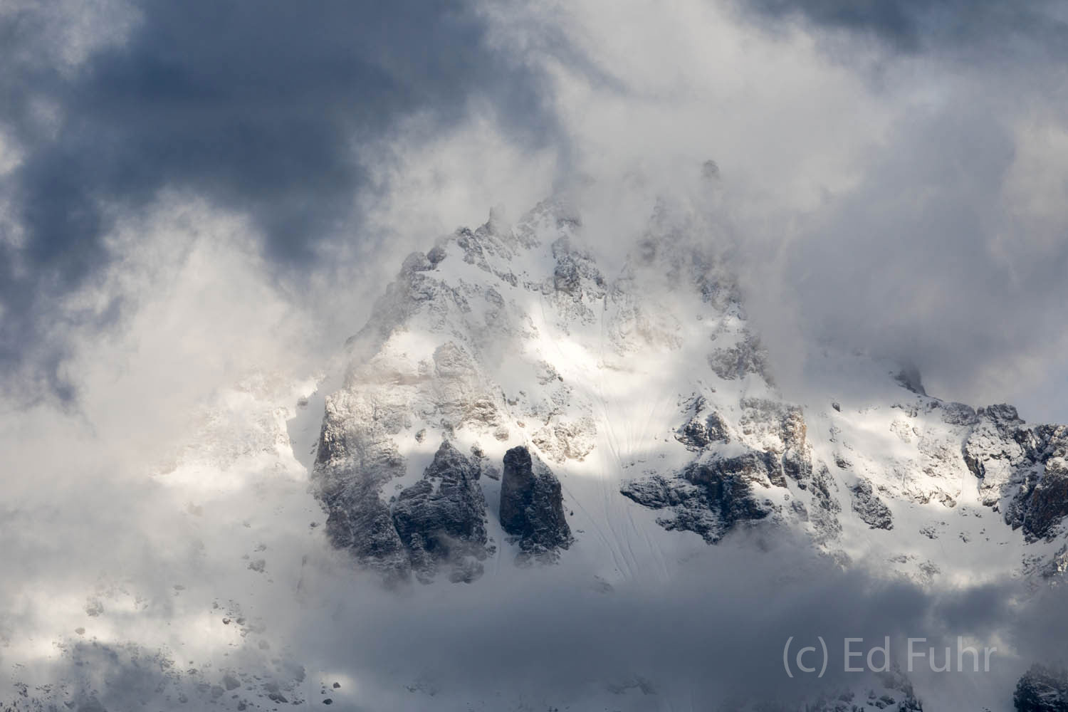 A window opens in the storm clouds allowing a peak at the Grand Teton, revealing that these clouds have delivered a June snow...