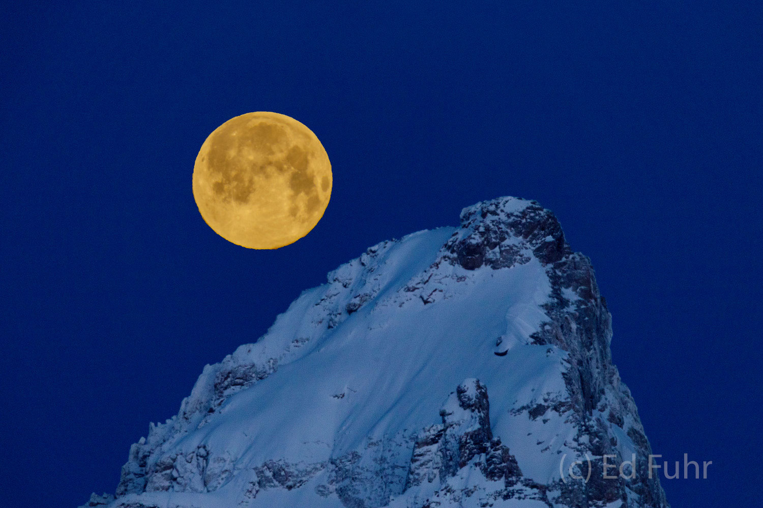 Just before sunrise, the air is crisp and clear.  It is more than 20 below and a super snow moon seems tethered to the Grand...