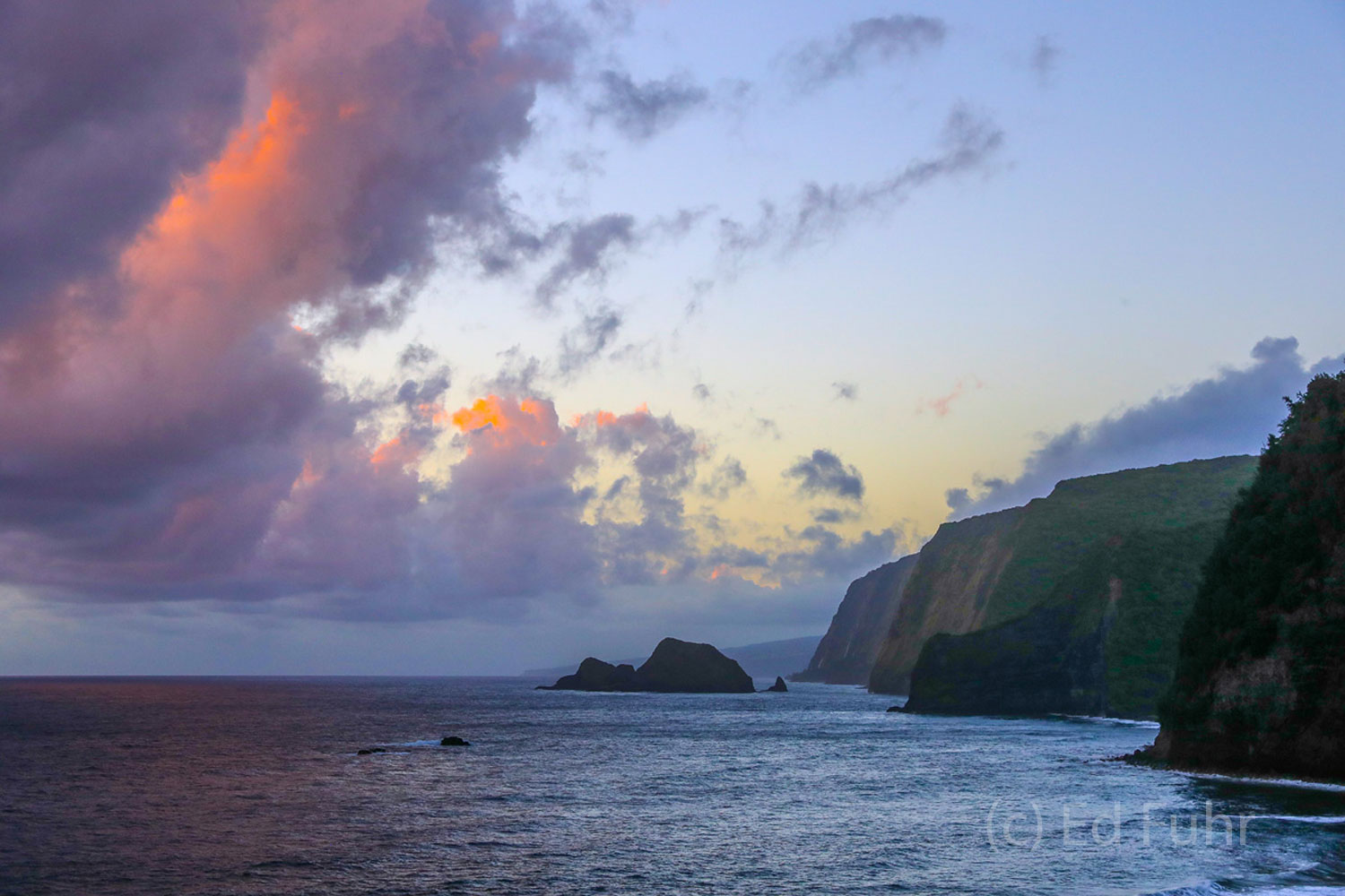 As the sun begins to emerge above the horizon, departing storm clouds above Pololu Valley turn orange and pink for a few moments...