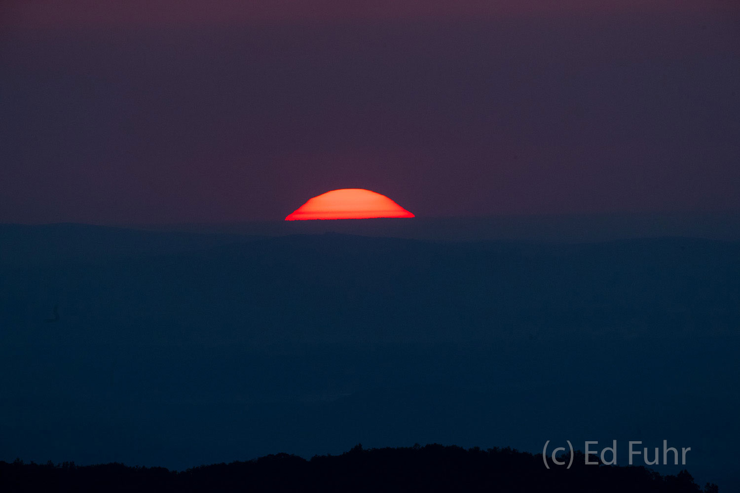 A blood red sun rises above the eastern horizon.
