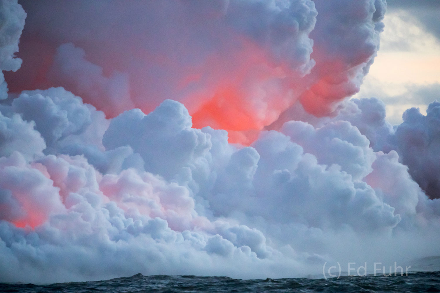 Below the soft steam cloud, the heat of the lava can be seen glowing brilliantly.