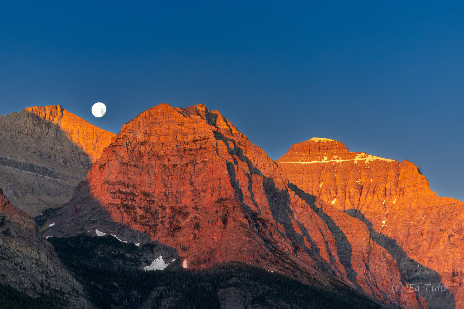A full moon sets above the mountains east of St. Mary's Lake.