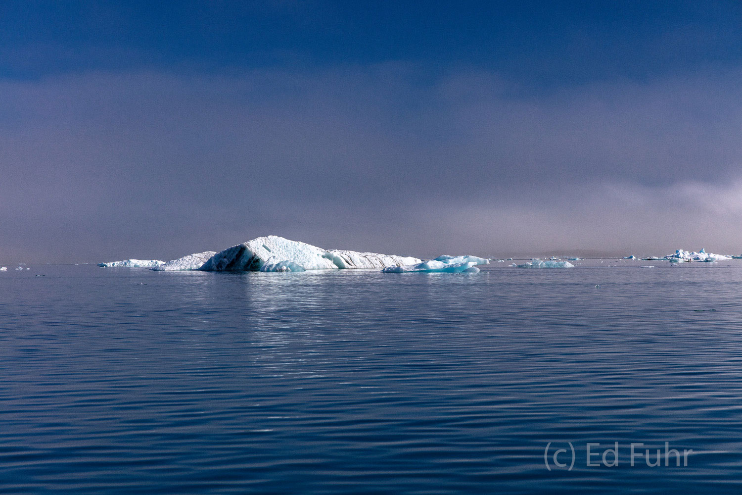 A light fog hovers above this lagoon as a iceberg shimmers in the distance.