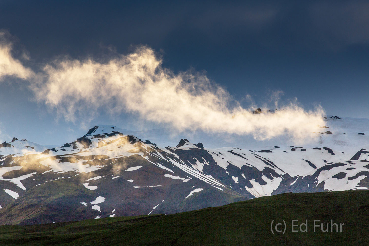 A long day of rain and clouds has given way and the final light of evening illuminates a rising wisp of cloud and fogs as it...