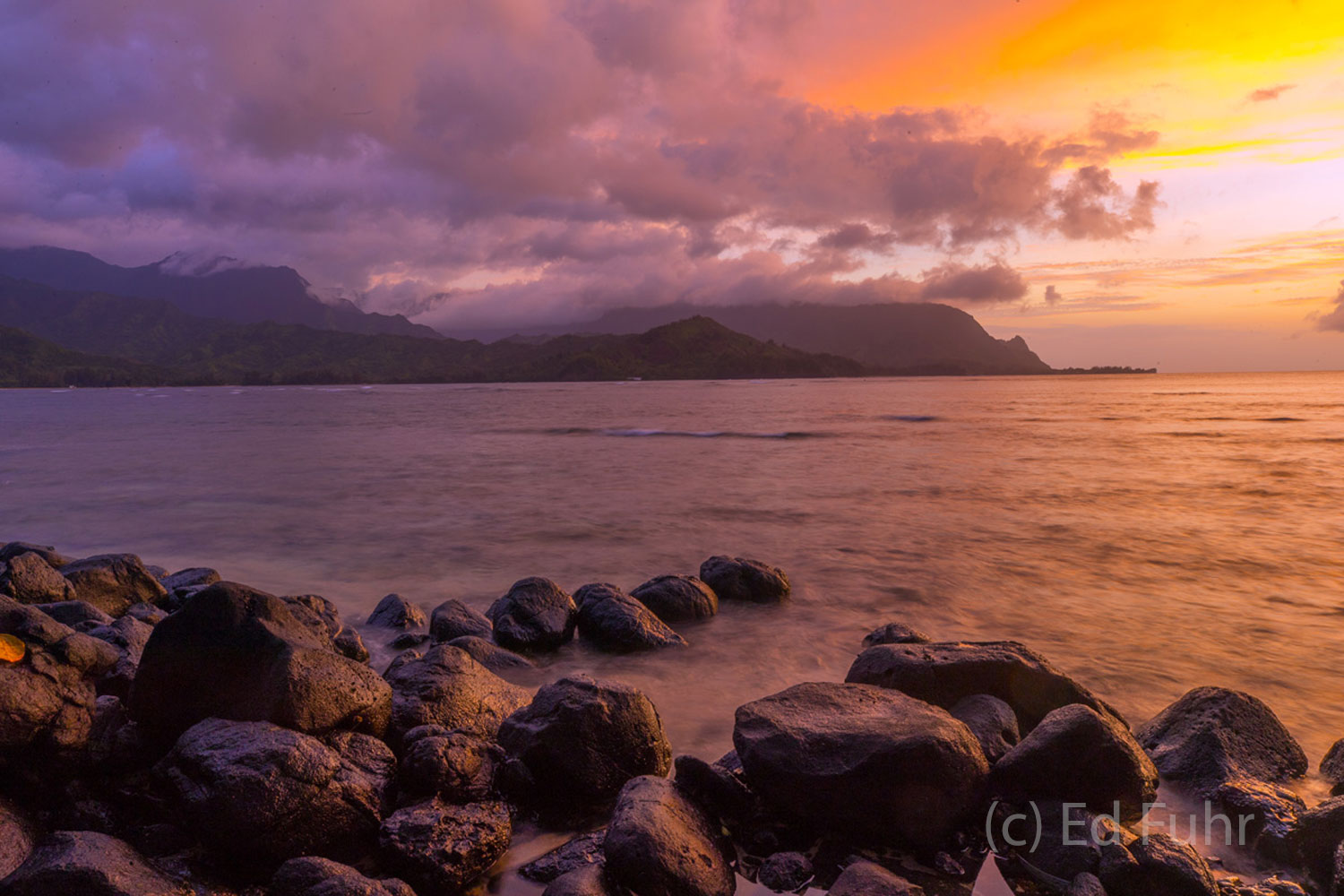 Sharp lava rocks contrast with the warm hues of sunset reflecting in Honalei Bay.