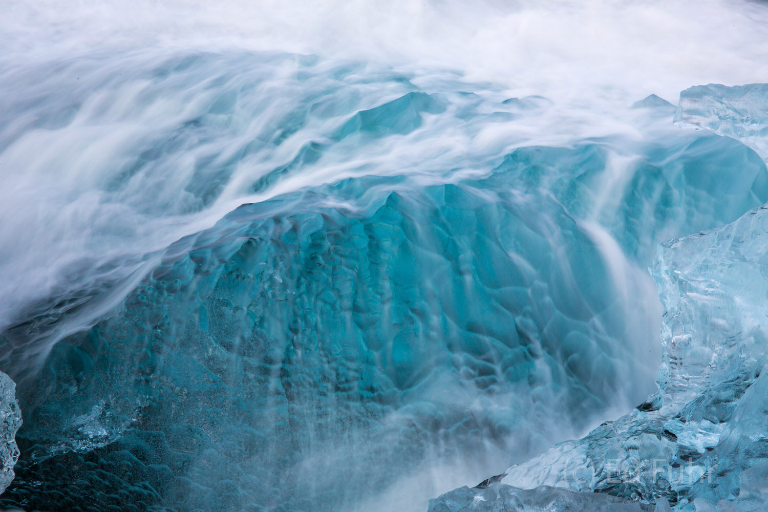 A soft waves cascades over this blue chunk of ice.