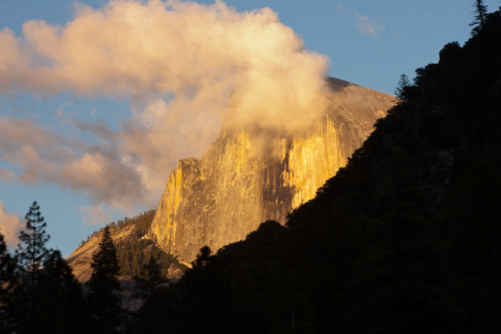 Behind a silhouetted ridge, Half Dome captures the last rays of light.&nbsp;