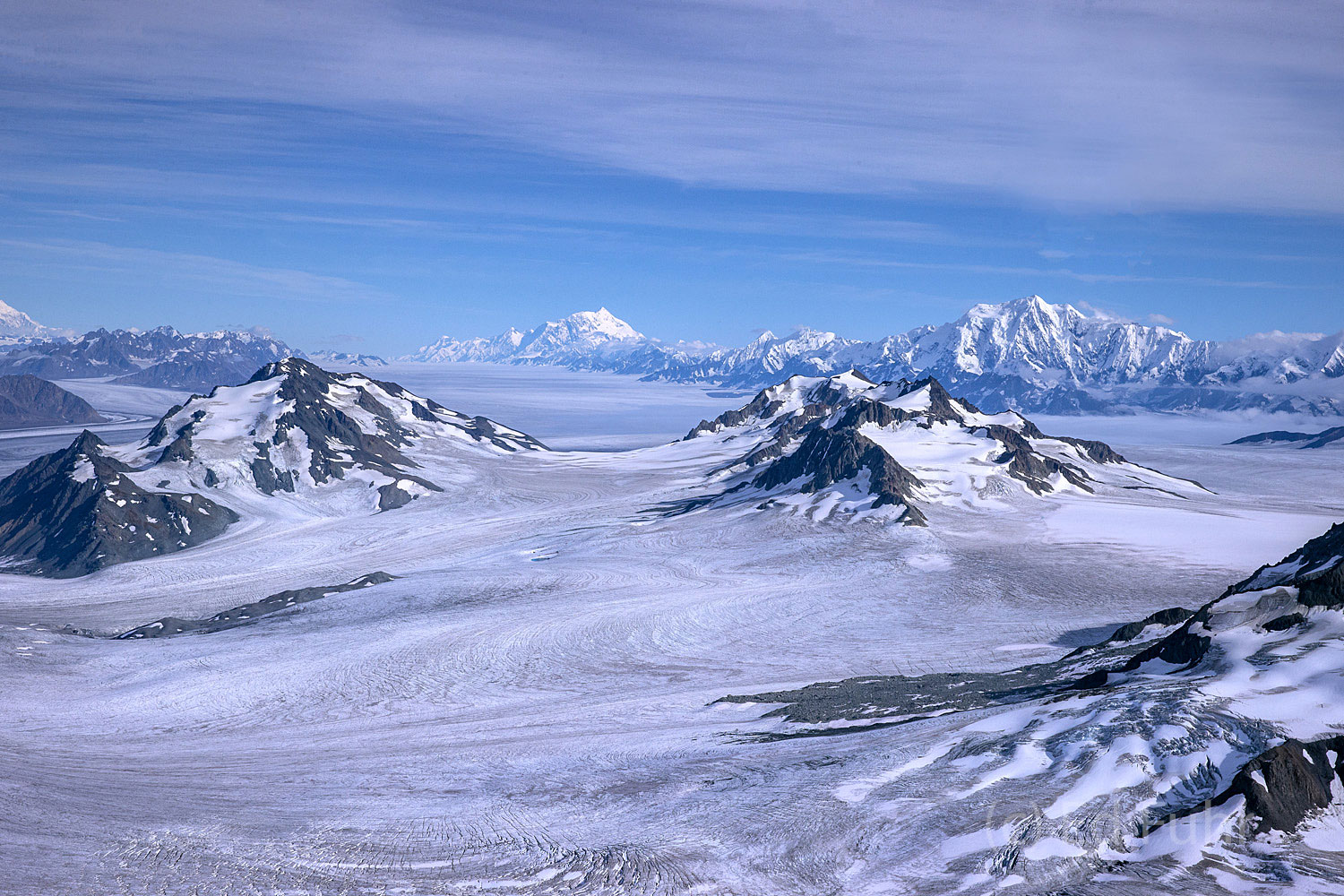 Enormous icefields stretch as far as the eye can see and are surrounded by massive Mounts Logan on the very far left, Mount St...