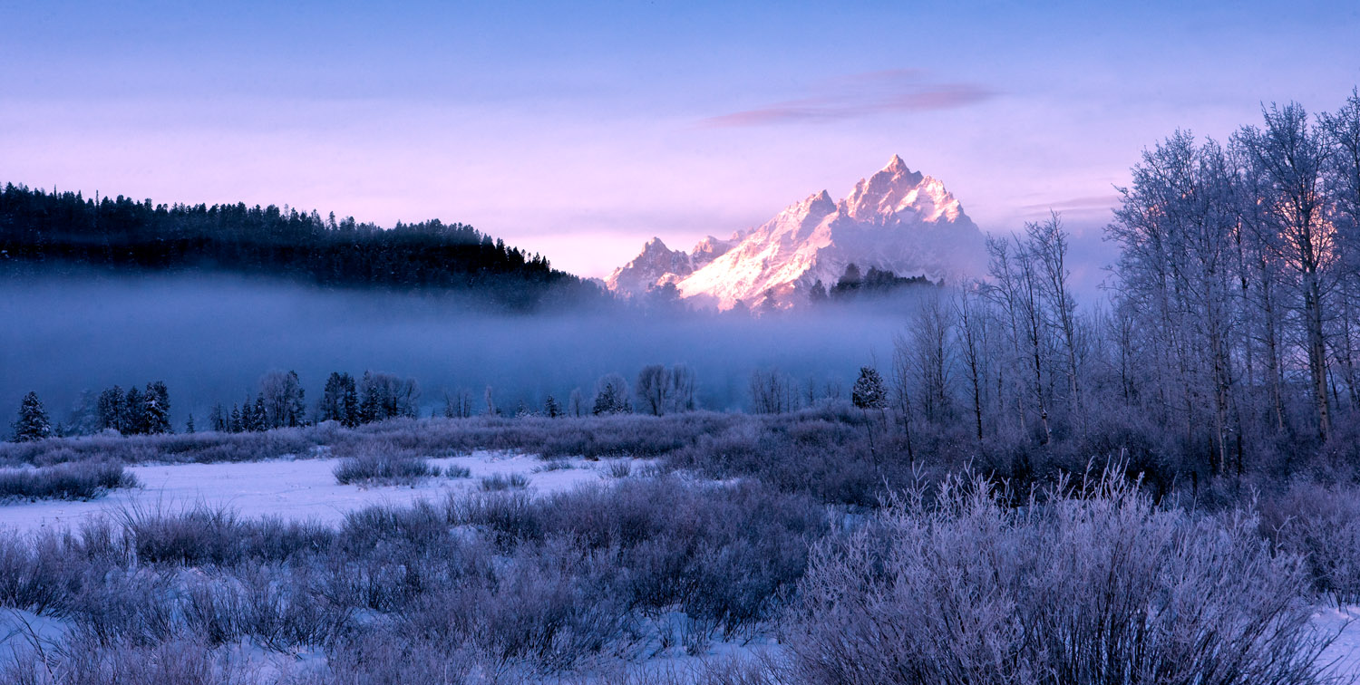 The Teton range peeks above the fog that hovers above the frozen Snake River.&nbsp;